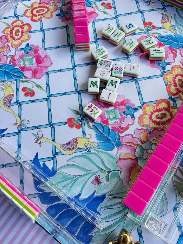 A close-up of a colorful floral mahjong game board with white tiles featuring green and multicolor symbols, arranged on a white background with pink and green accents.